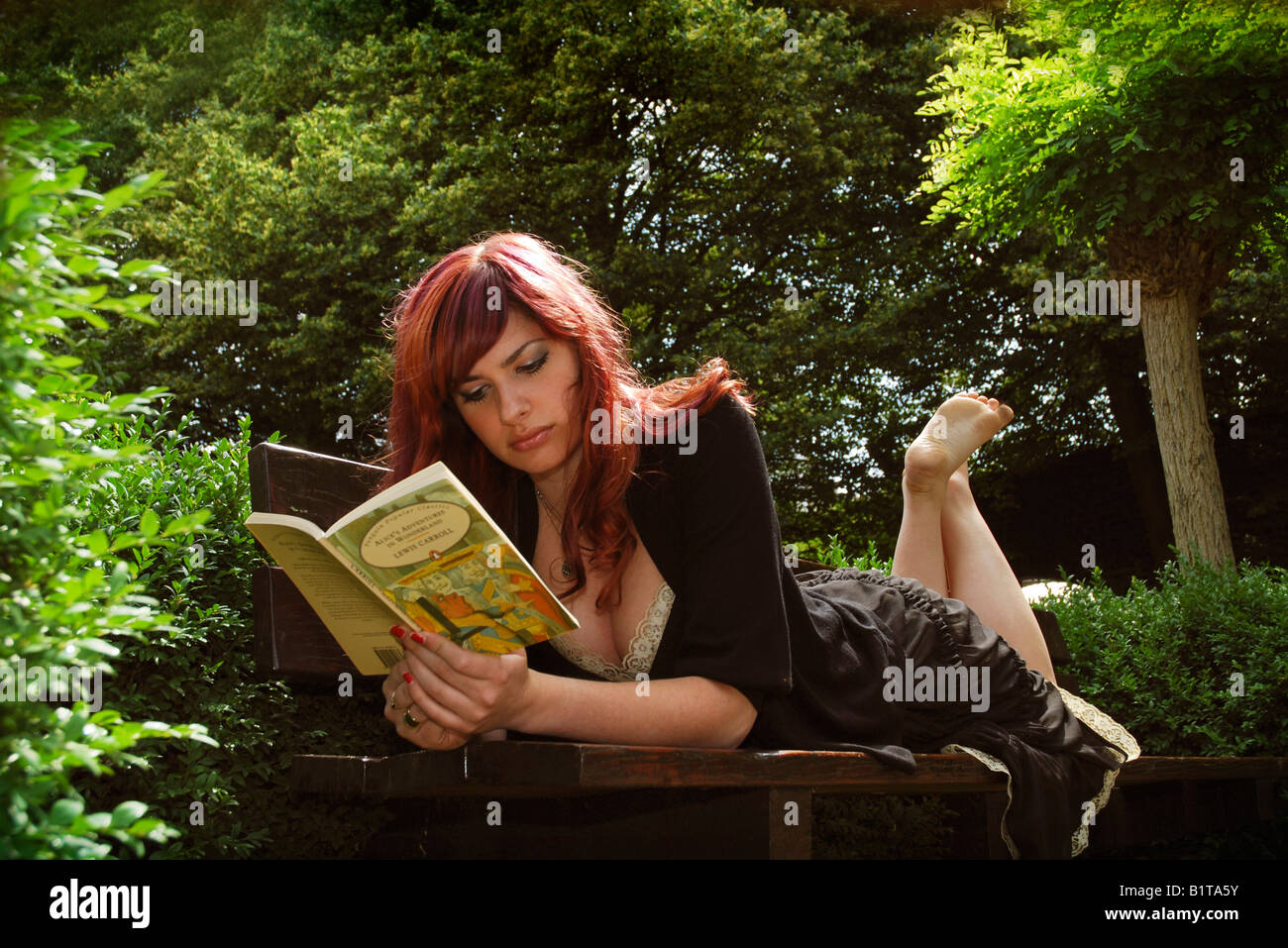 barfuß Mädchen Alice im Wunderland auf einer Parkbank sitzend lesen Stockfoto