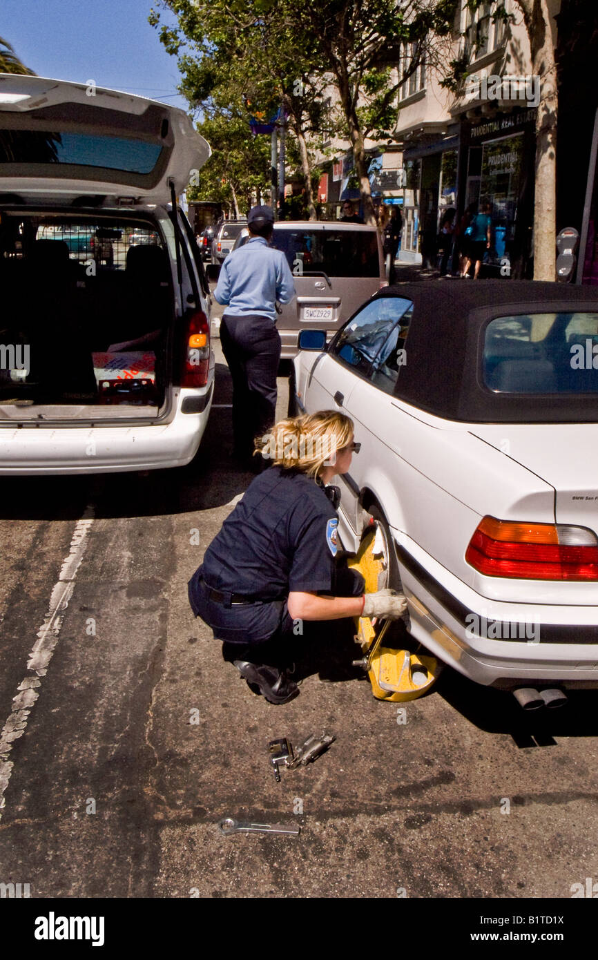Ein Parkplatz Vollzugsbeamten installiert ein Rad Wegfahrsperre oder Boot auf ein Auto mit hervorragenden Parkplatz Verletzungen in San Francisco Stockfoto