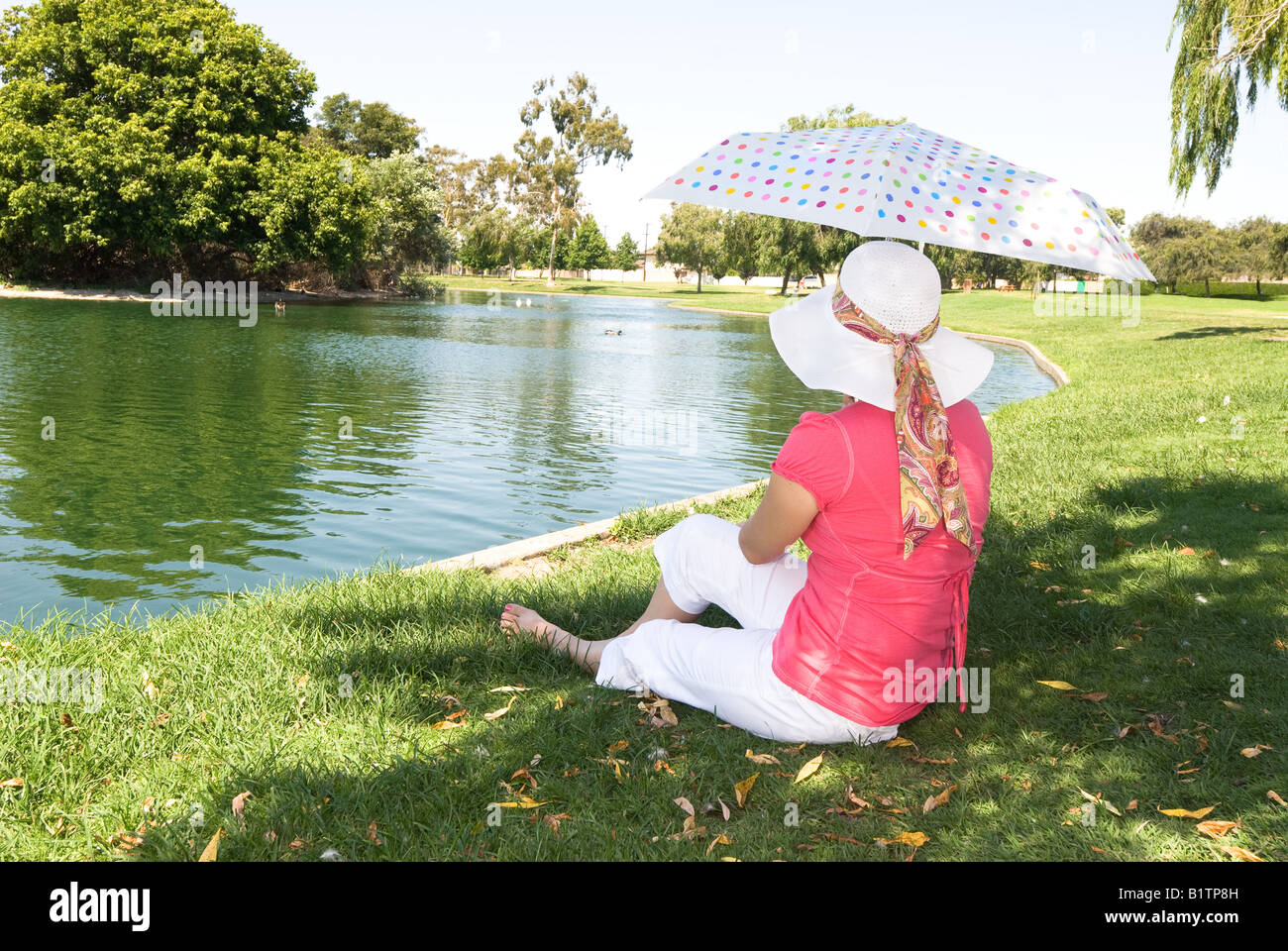 Eine Frau liegt an einem Park-See während der Verwendung eines bunten Regenschirm um sich vor der Sonne schützen Stockfoto