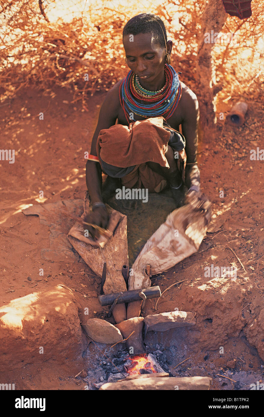 Samburu Frau arbeitet Ziegenleder Blasebalg Luft in das Kohlenfeuer für Ehemann Schmied nördlichen Kenia in Ostafrika Stockfoto