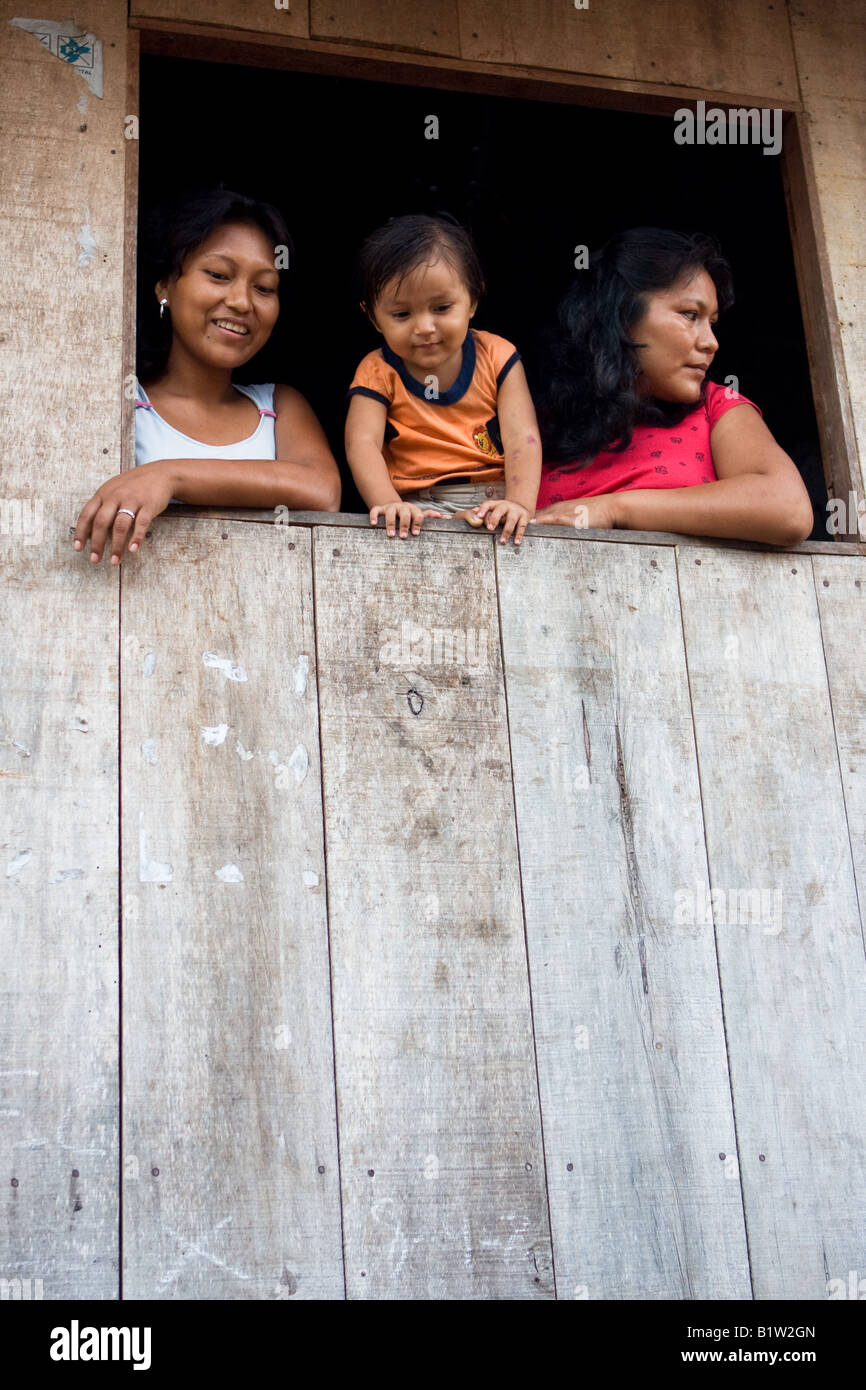 Eine peruanische Mutter und ihre zwei Kinder lehnen aus ihrem offenen Fenster auf Isla Iquitos, einer Insel im Amazonas-Flusses in der Nähe von Iquitos. Stockfoto