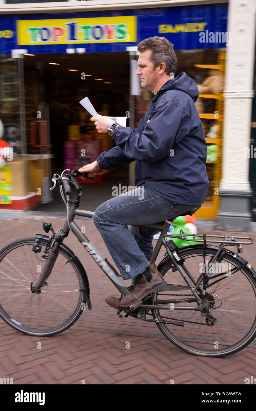 Ein Radfahrer, lesen und Radfahren entlang der Fahrbahn. Delft. Niederlande. Stockfoto