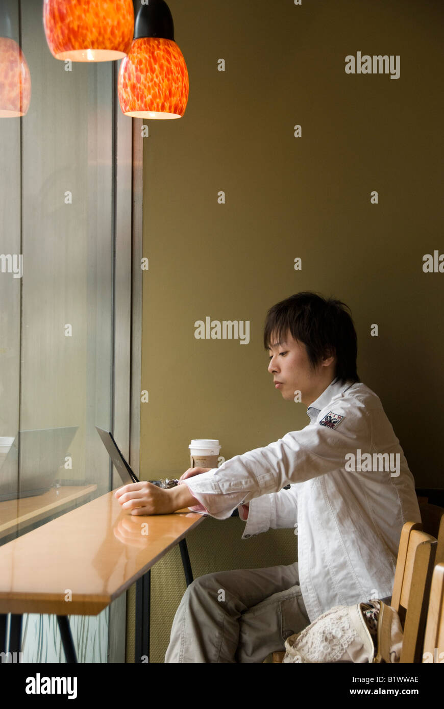 Kyoto, Japan. Ein junger Mann, der an einem Notebook arbeitet mit dem Computer kostenloses Wlan in einer Filiale von Starbucks Coffee Shop Stockfoto