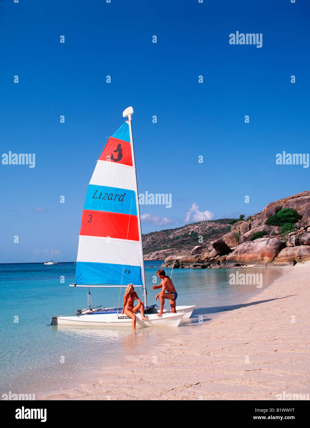 Zwei Personen bereiten ein kleines farbenfrohes Segelboot an einem ruhigen tropischen Strand mit klarem blauem Himmel vor Stockfoto