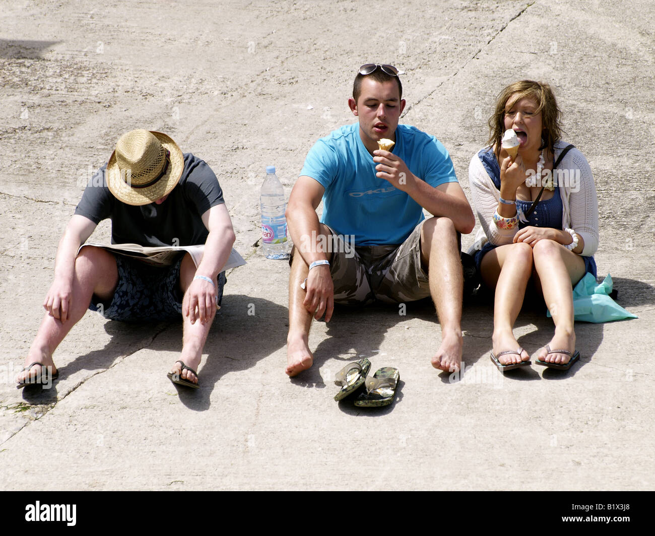 Drei junge Leute, zwei essen Eiscreme und eine Zeitung lesen Stockfoto