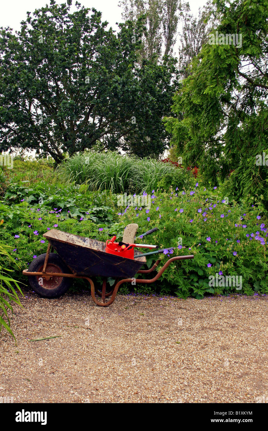 SCHUBKARRE UND WERKZEUGE IN EINEM LAUSCHIGEN GARTEN. Stockfoto