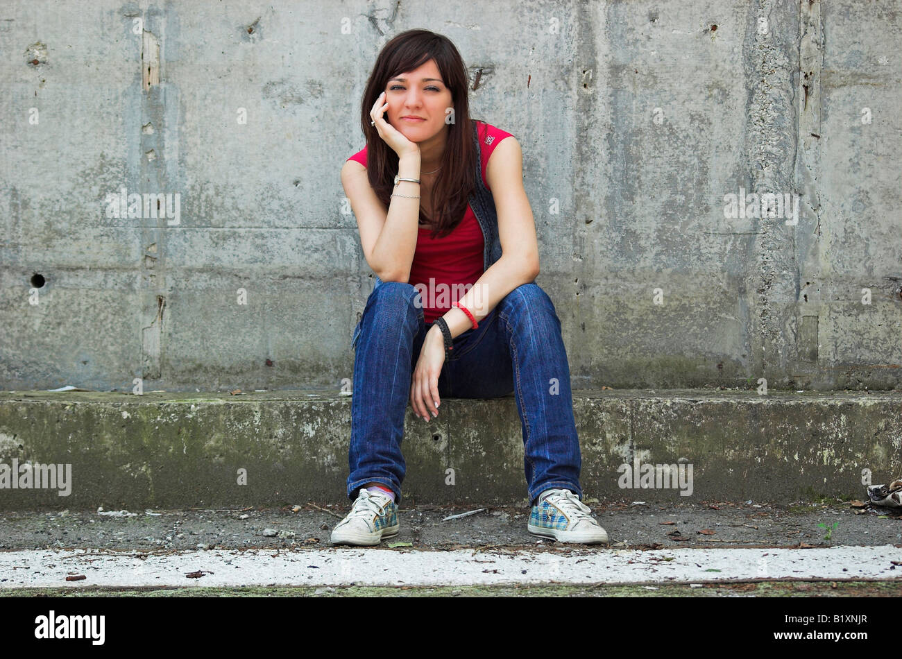 Porträt der jungen Frau sitzt vor einem Zement Wand Kopf in Händen Stockfoto