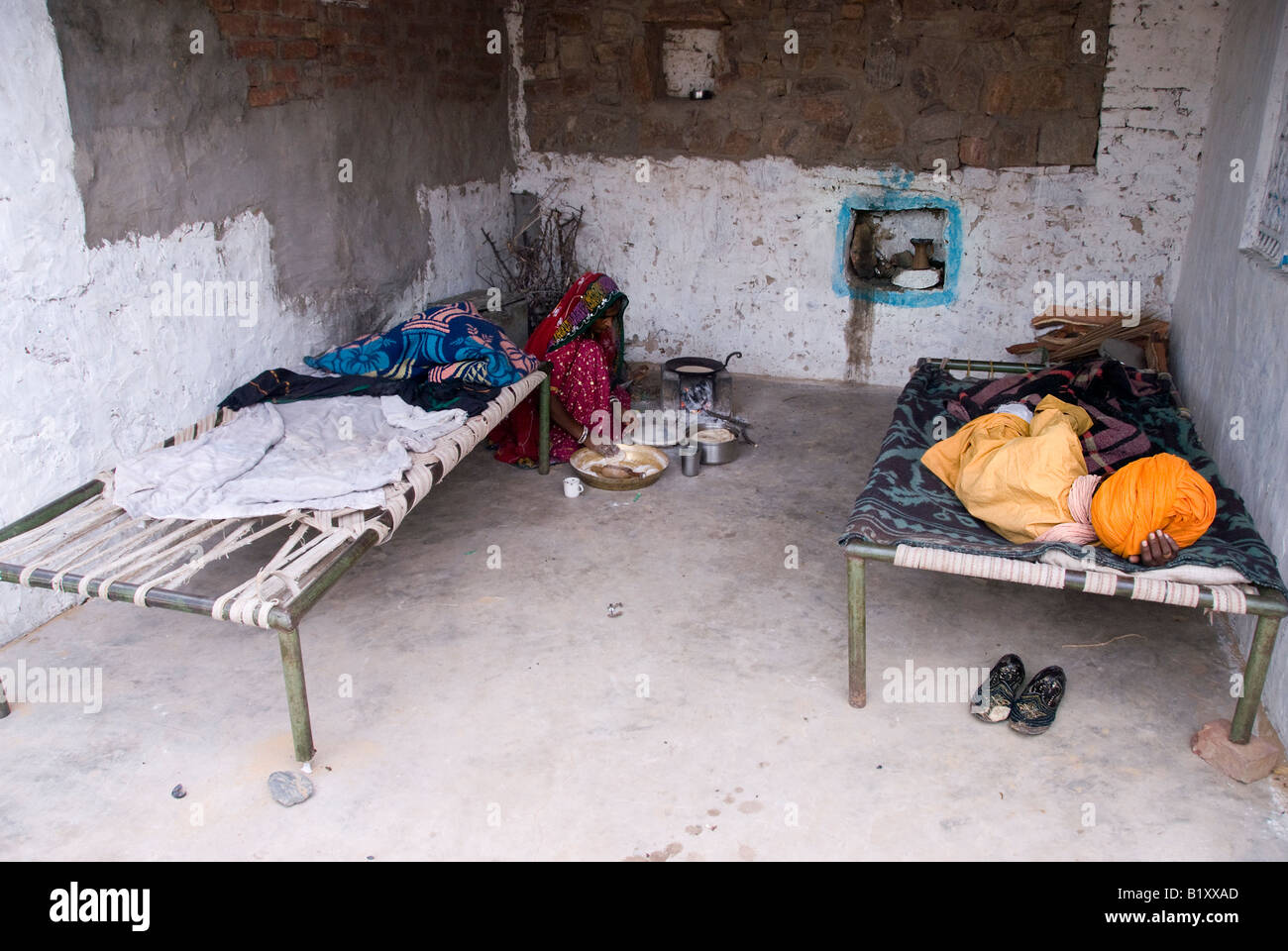 Rajasthani Frau bereitet Essen, während ihr Schwiegervater im gleichen Hof, Rajasthan, Indien schläft. Stockfoto