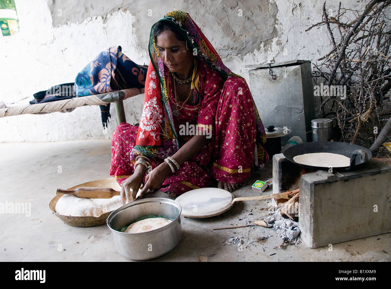 Frau aus Rajasthan (Indien) bereitet Essen. Kochen auf traditionellen Herd im Hof des Hauses. Typische Kleidung und Gefäße. Stockfoto