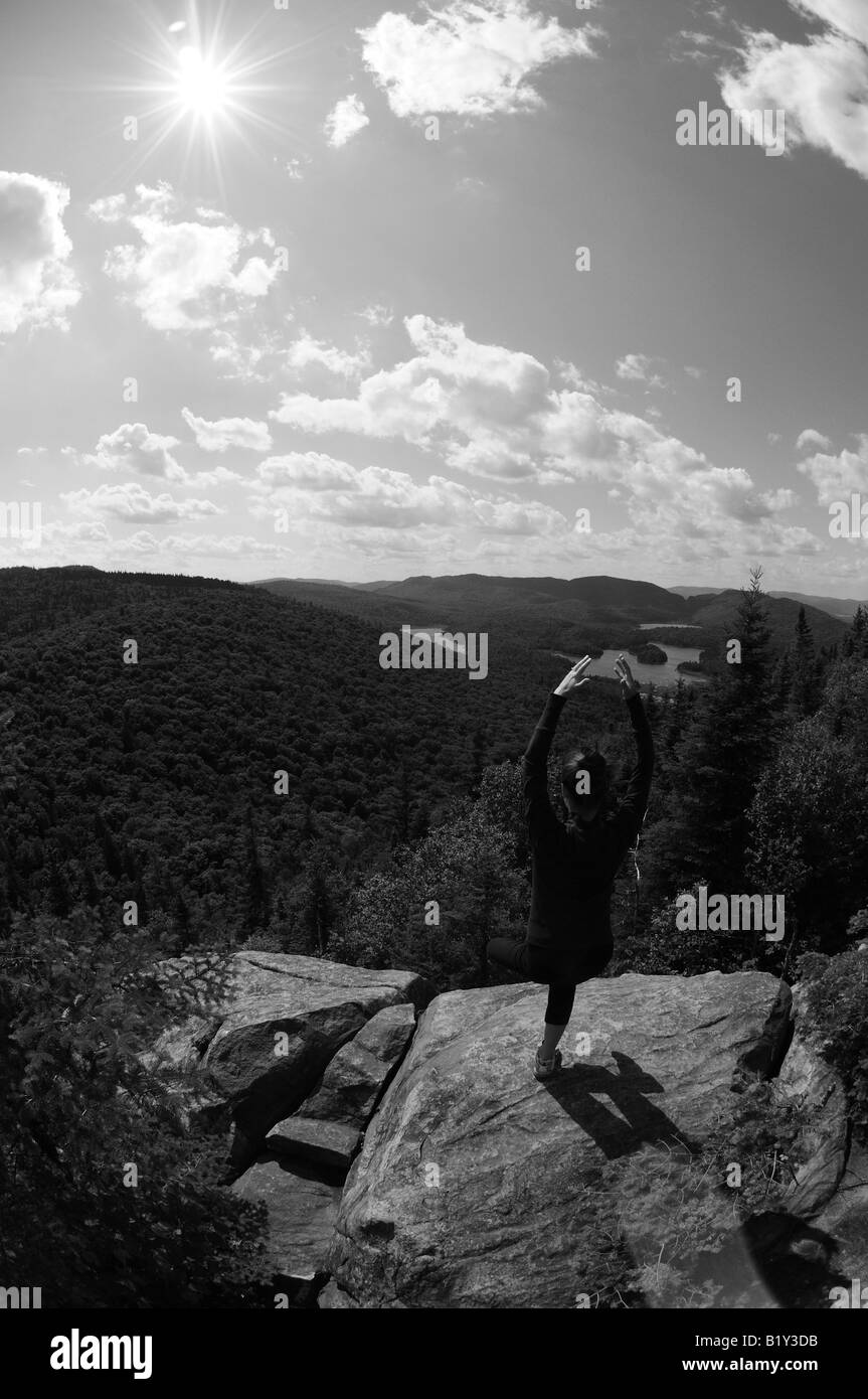 Ein schwarz-weiß, Weitwinkel-Foto einer Frau beim Yoga auf der Spitze einer Klippe erreichen für den Himmel mit ausgestreckten Armen Stockfoto