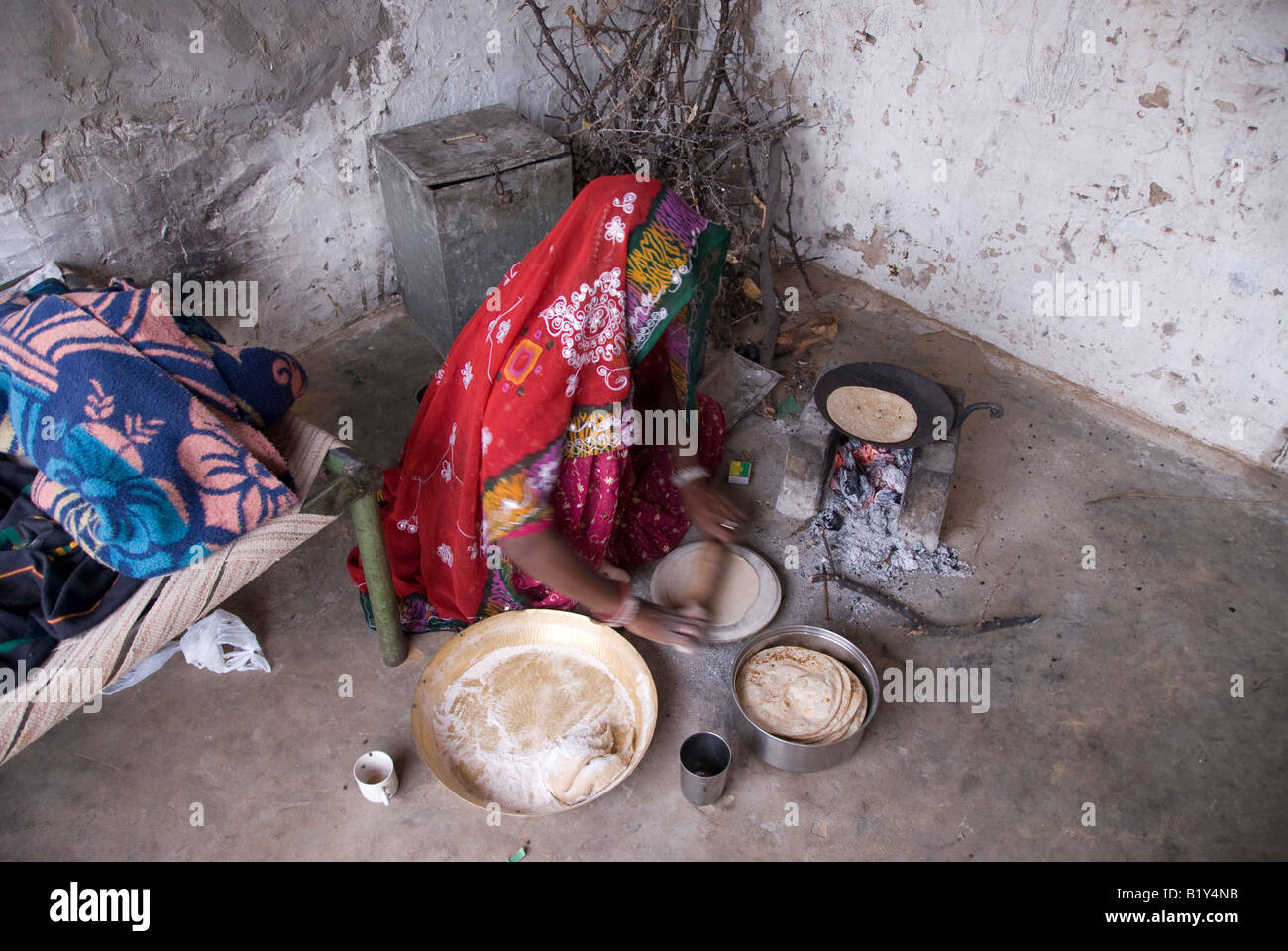 Frau aus Rajasthan (Indien) bereitet Essen. Kochen auf traditionellen Herd im Hof des Hauses. Typische Kleidung und Gefäße. Stockfoto