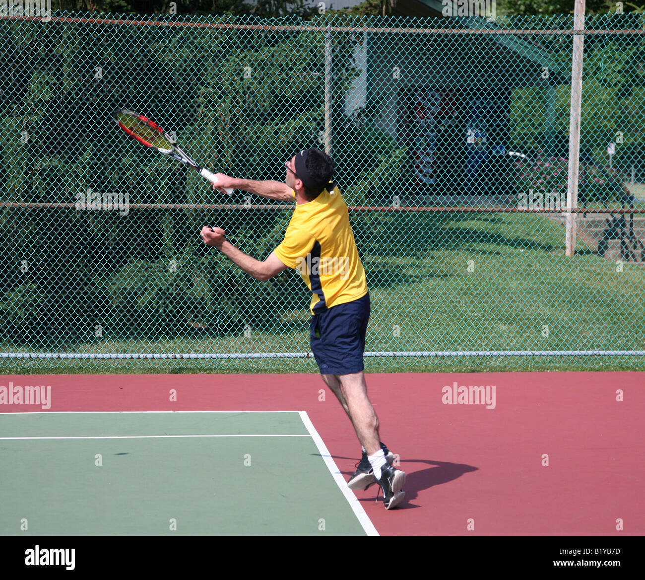 Ein junger Mann in einem gelben Hemd mit dem Tennisspielen. Stockfoto