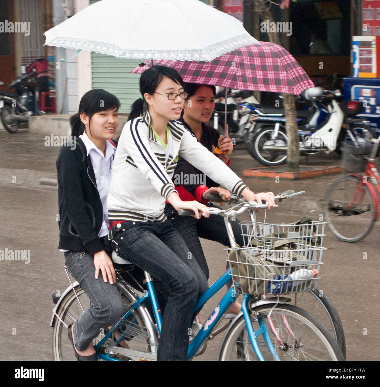 Mädchen auf dem Fahrrad Radfahren im Regen mit Sonnenschirmen, Halong Bucht, Vietnam Stockfoto