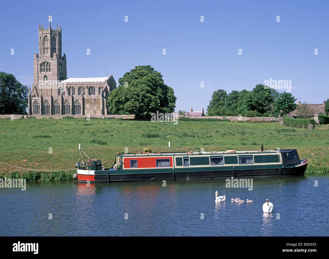 Ländliche Flusslandschaft Fotheringhay Dorfkirche St. Mary & All Saints festgemacht Narrowboot auf dem Fluss Nene Schwan & Cygnets Northamptonshire England GB Stockfoto