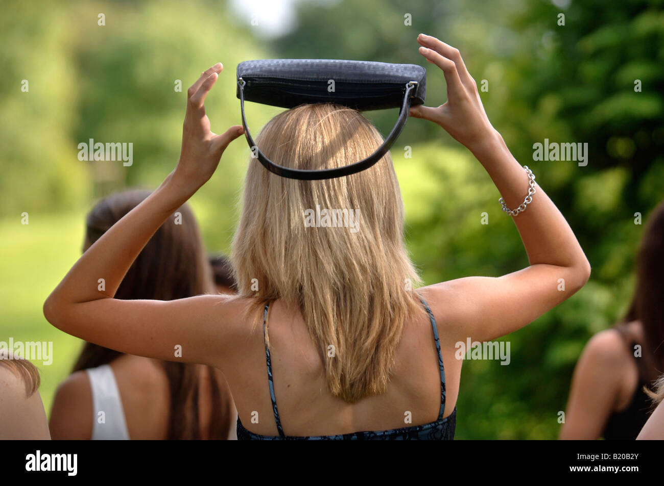 EINE JUNGE FRAU IN EINEM PARTYKLEID GLEICHT IHRE HANDTASCHE AUF DEM KOPF AN EINEN SOMMERGARTEN FUNKTION UK Stockfoto