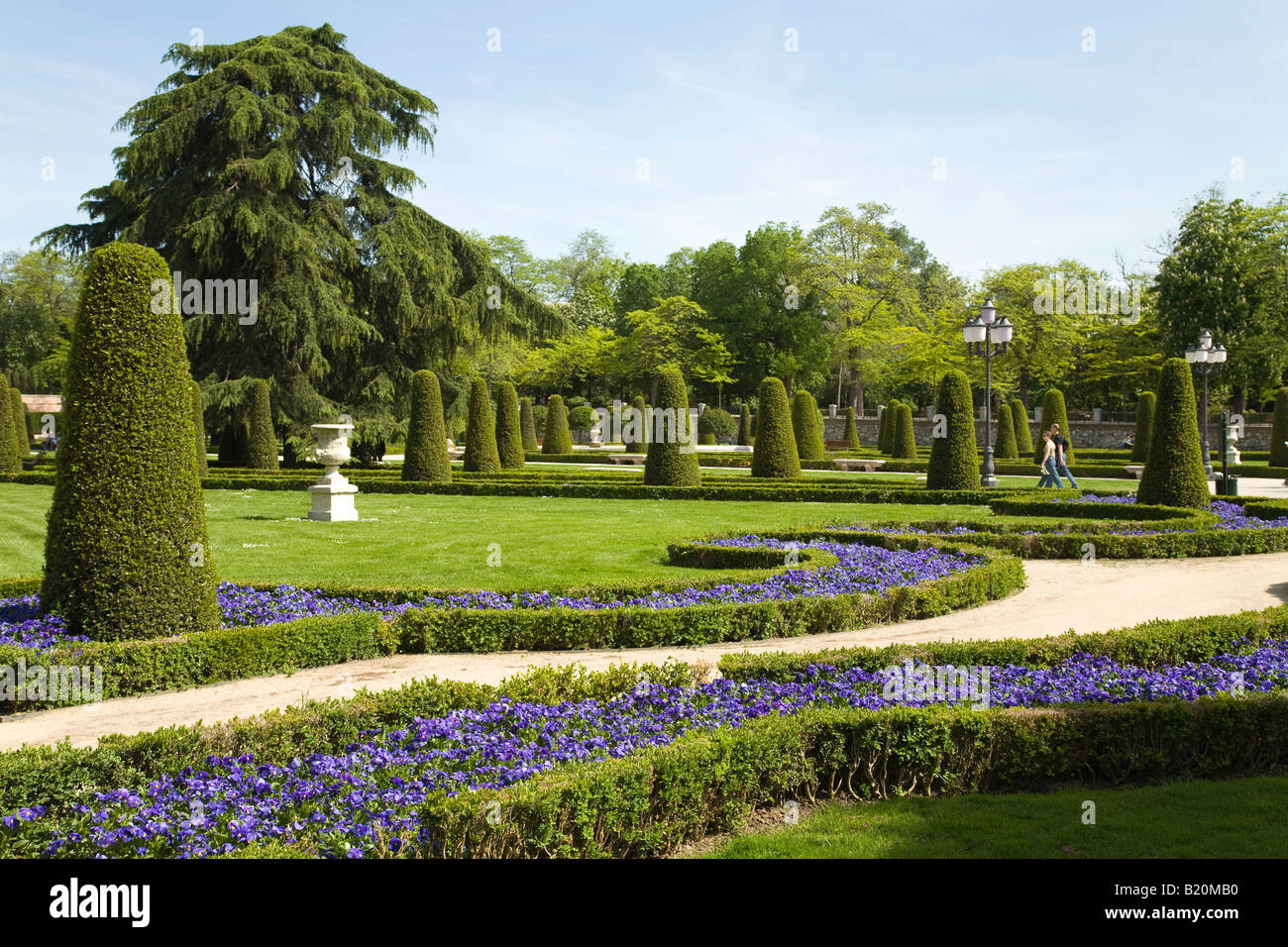 Spanien Madrid Menschen gehen auf Bürgersteig durch Gärten im Retiro Park Parque del Buen Retiro, geformte Sträucher und Blumen Stockfoto