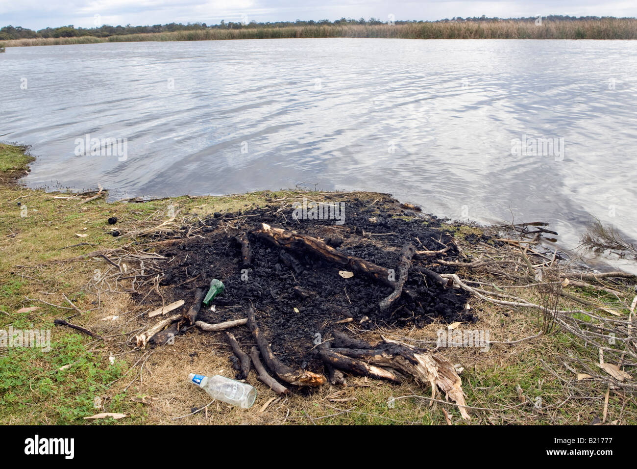 A Feuer und weggeworfene Bierflaschen am Ufer eines Sees ausgebrannt. Stockfoto