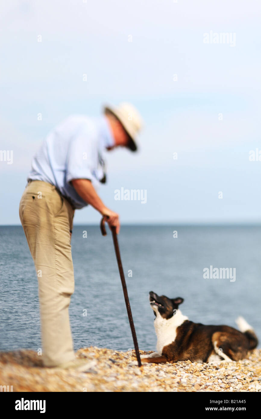 älterer Mann mit Spazierstock Stand am Strand mit Hund Stockfoto