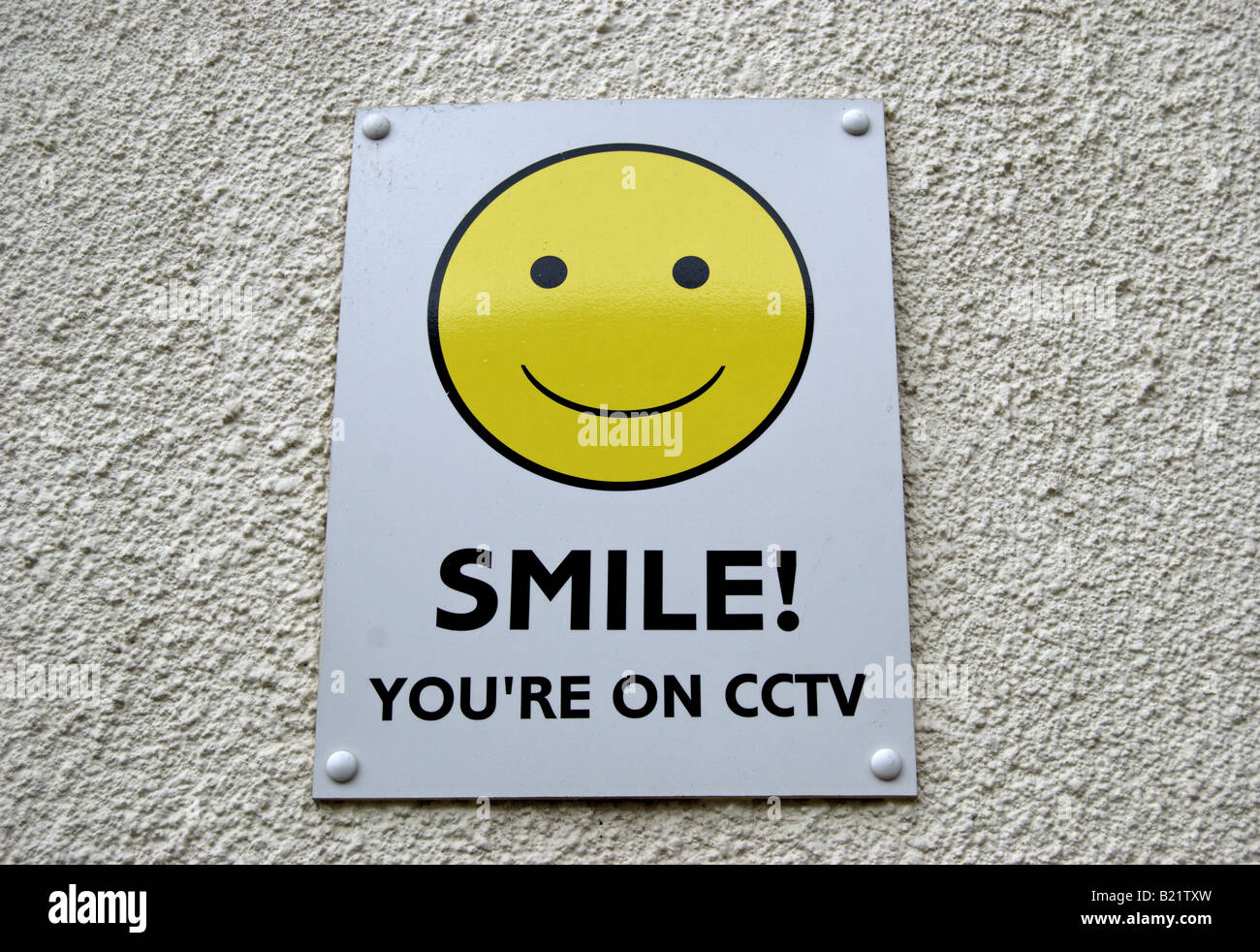 britische cctv-Warnschild mit gelben Smiley-Gesicht auf weißen strukturierte Wand Stockfoto