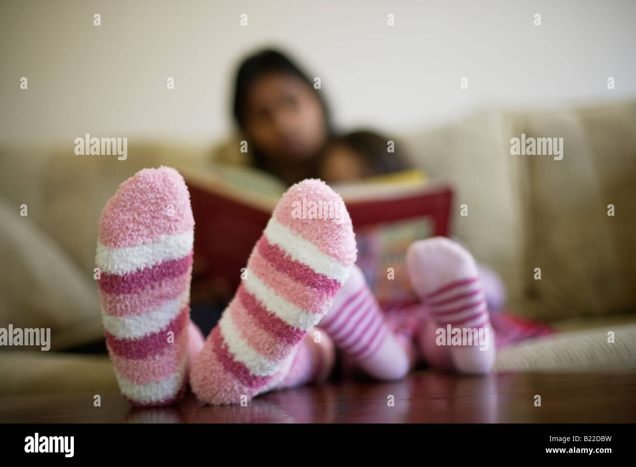 Indische Mutter der 30er Jahre und Mischlinge Tochter 4 lesen Sie ein Buch rosa gestreifte Socken Stockfoto
