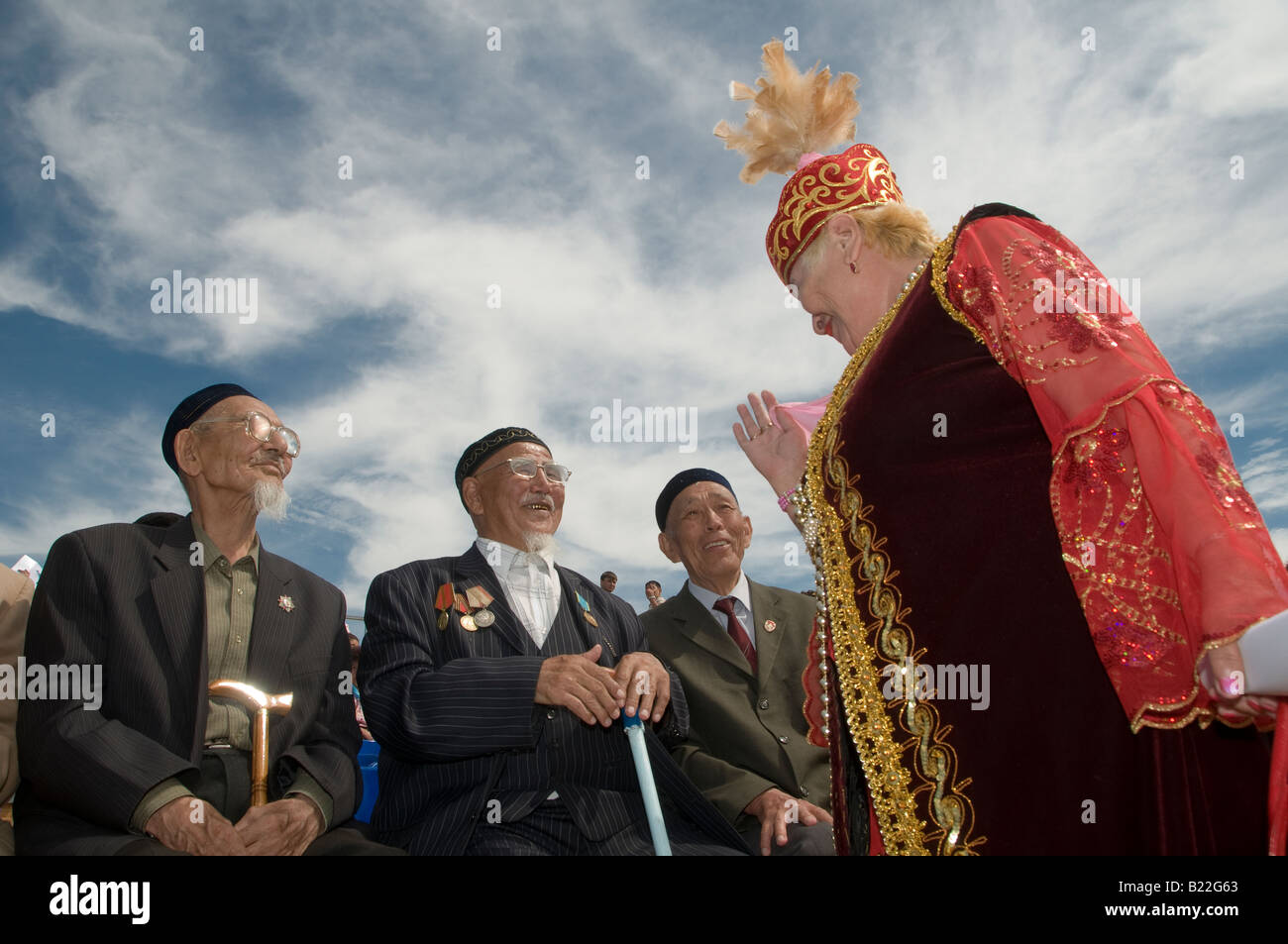 Eine Frau in traditioneller kasachischer Shapan-Kleidung unterhält sich mit Veteranen, die sowjetische Kriegsmedaillen trugen, die im Zweiten Weltkrieg in Kasachstan kämpften Stockfoto