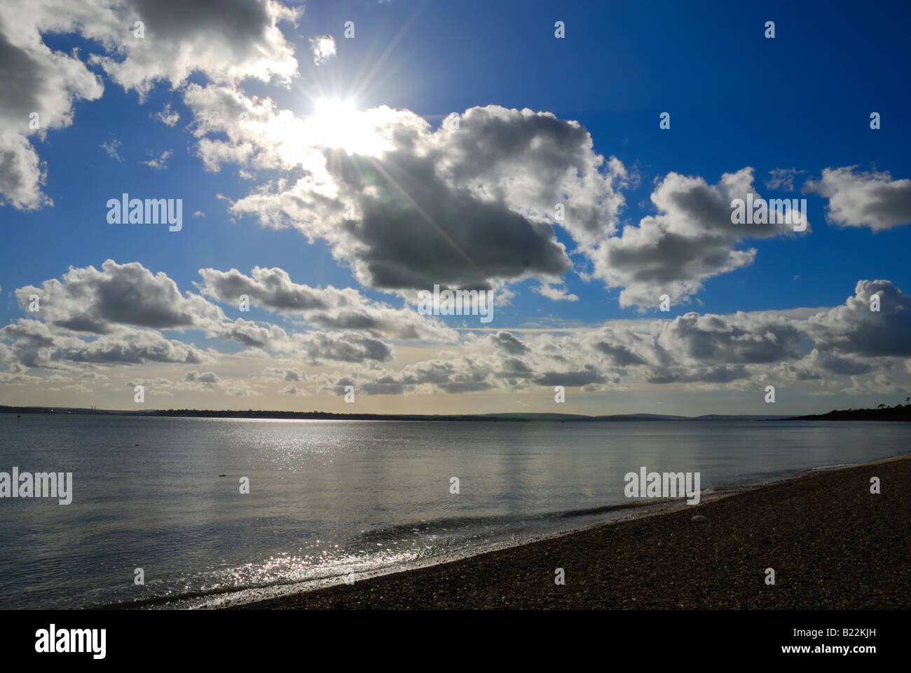 Sun durch Wolken mit Strand und Meer im Vordergrund Calshot Hampshire England Großbritannien Stockfoto