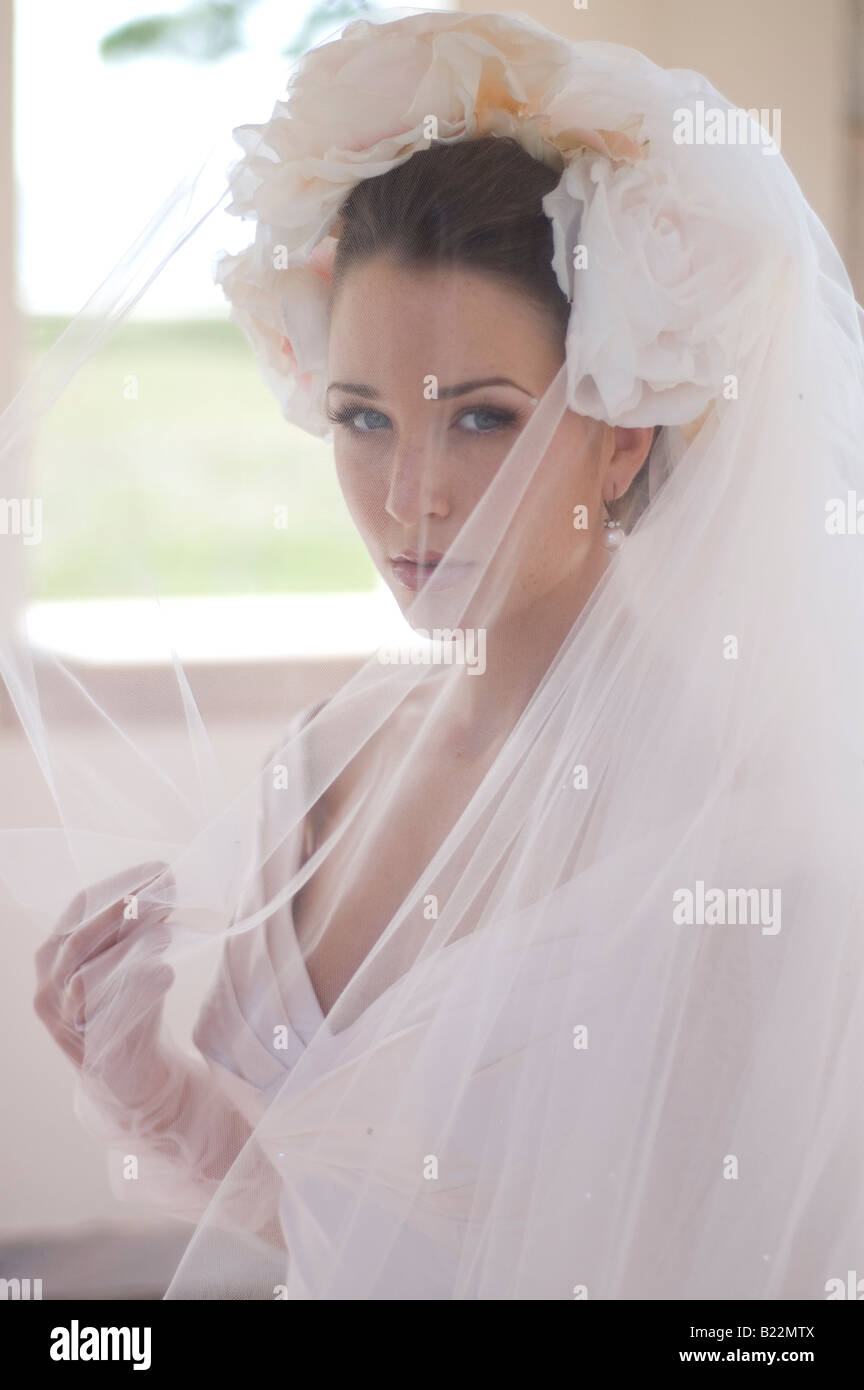 Eine schöne junge Braut in einem rosa Kleid und floralen Kopfschmuck Blick durch ihren Schleier. Stockfoto