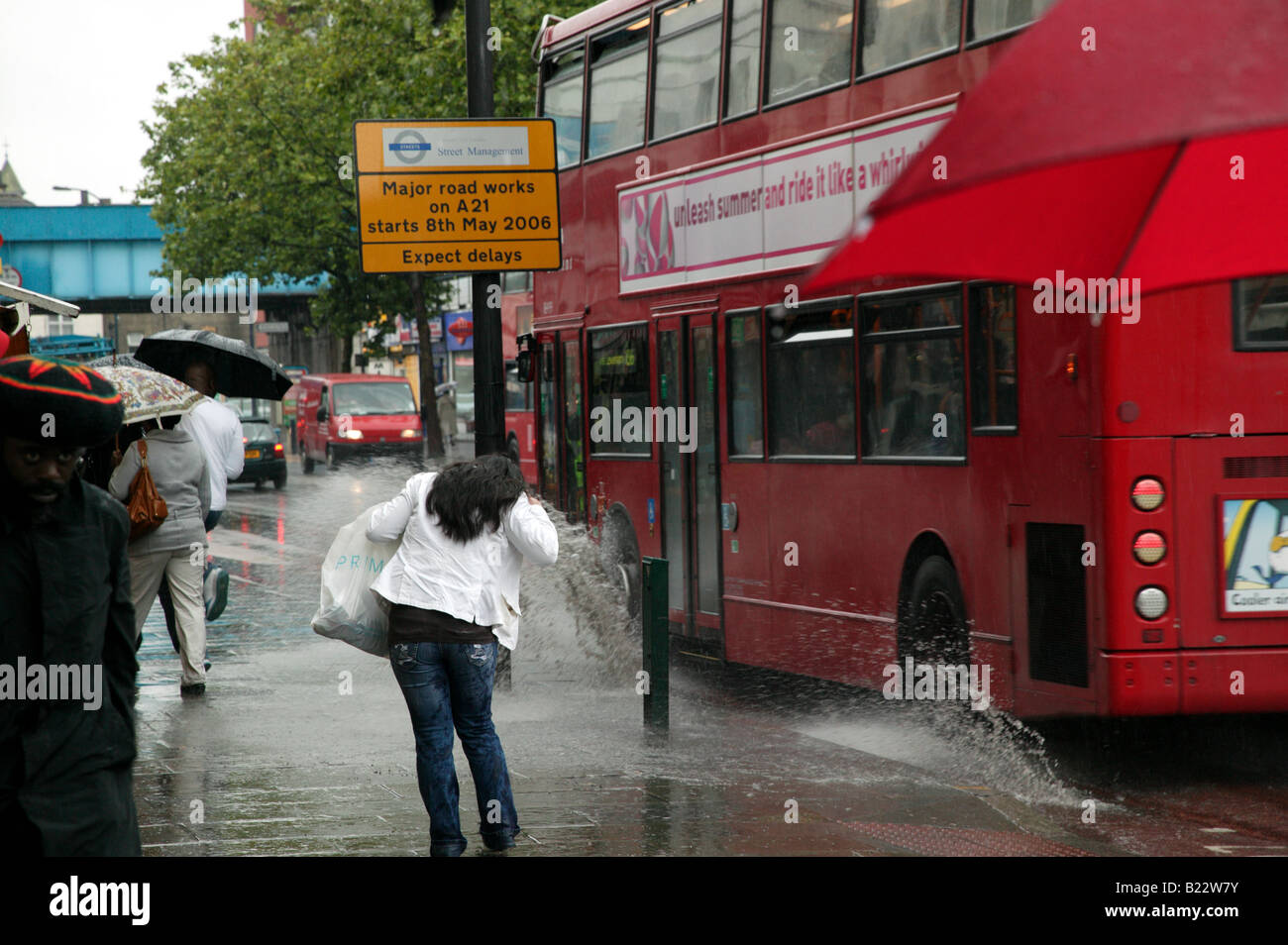 Frau, die versucht zu vermeiden, wird von einem vorbeifahrenden Bus auf Lewisham Hautpstraße spritzte. Stockfoto