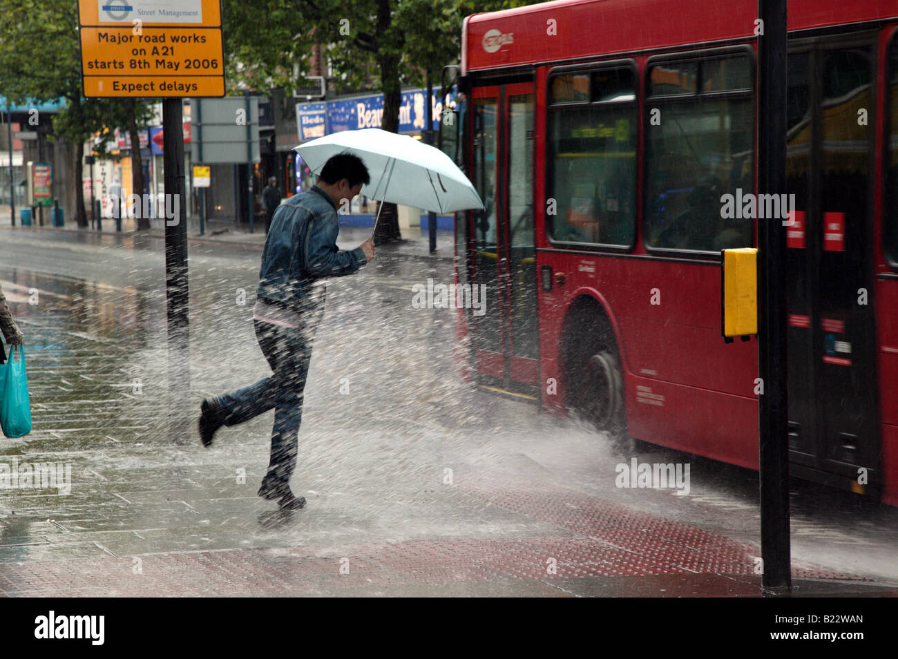 Mann wird von einem vorbeifahrenden Bus auf Lewisham Hautpstraße an einem sehr regnerischen Tag gespritzt Stockfoto