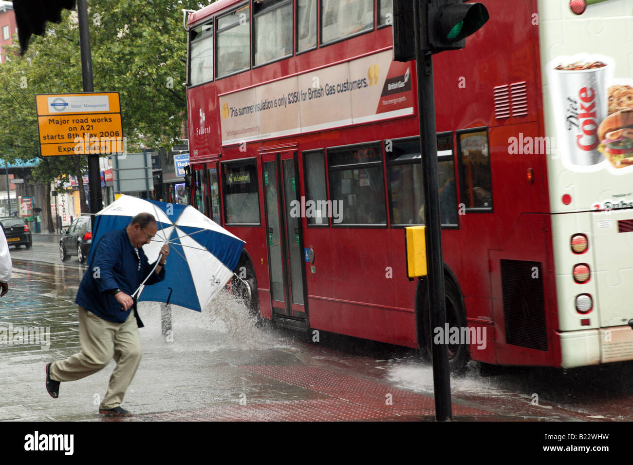 Regentanz: Ein Mann vermeidet wird von einem vorbeifahrenden Bus auf Lewisham Hautpstraße an einem sehr regnerischen Tag gespritzt Stockfoto