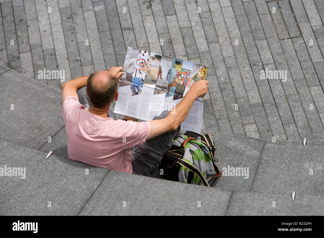Eine Glatze Mann wahrscheinlich ein Tourist hält einen Reiseführer in die Schaufel außerhalb von London City Hall sitzen Stockfoto