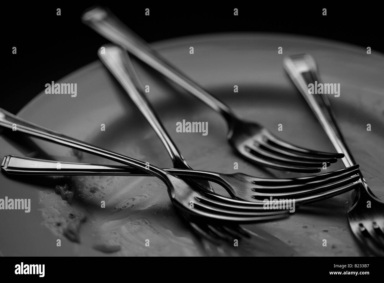 Schwarz / weiß Bild von einem leeren Teller mit fünf Gabeln Stockfoto