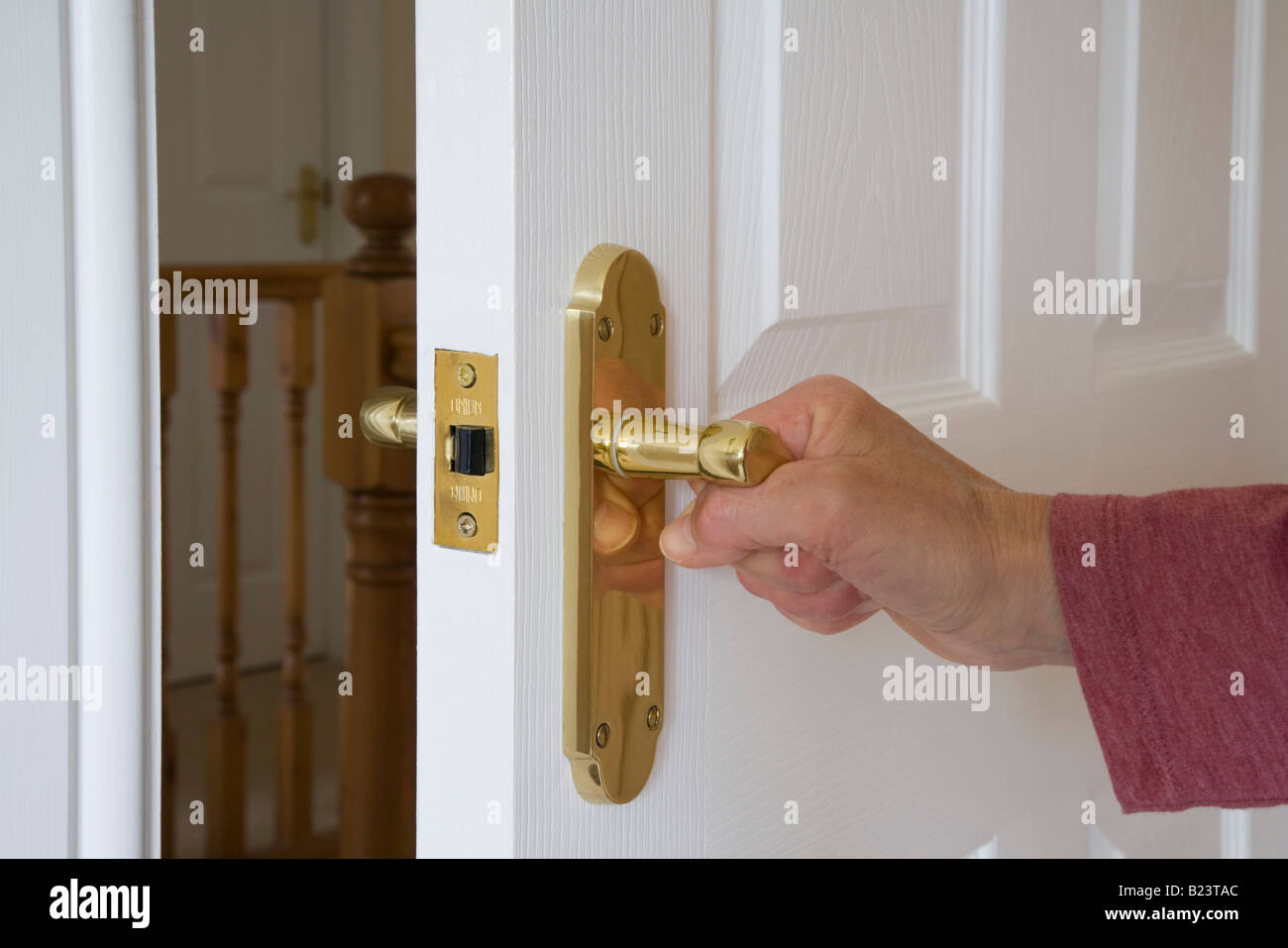 Frau öffnet oder schließt eine weiße Holztür Drehgriff mit Hand auf Gold Riegel oben Zimmer. England Großbritannien Stockfoto