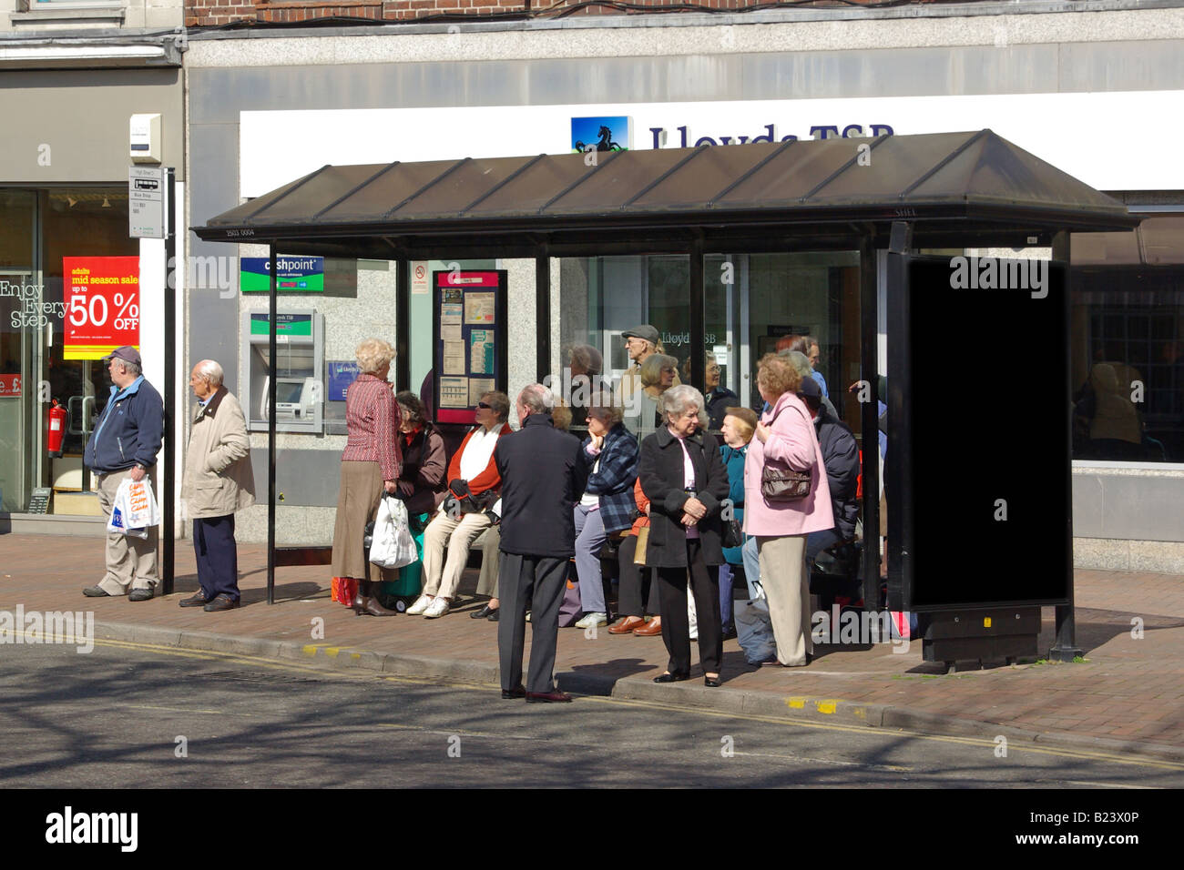 Menschen warten an der Bushaltestelle in High Einkaufsstraße außerhalb Lloyds Bank Stockfoto