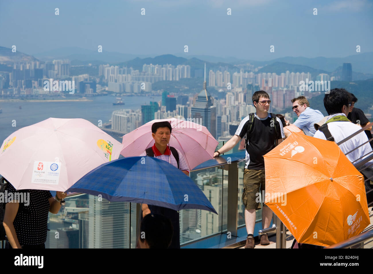 Touristen mit des Regenschirmes Blick auf Hong Kong Panorama von der Aussichtsterrasse des Victoria Peak Tower an einem heißen sonnigen Tag. Stockfoto