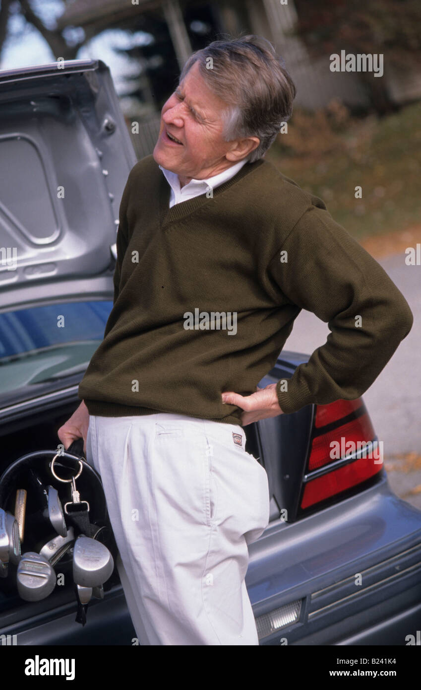 MANN MIT NIEDRIGEREN RÜCKSEITIGEN SCHMERZ LADEN GOLF CLUBS IN AUTO Stockfoto