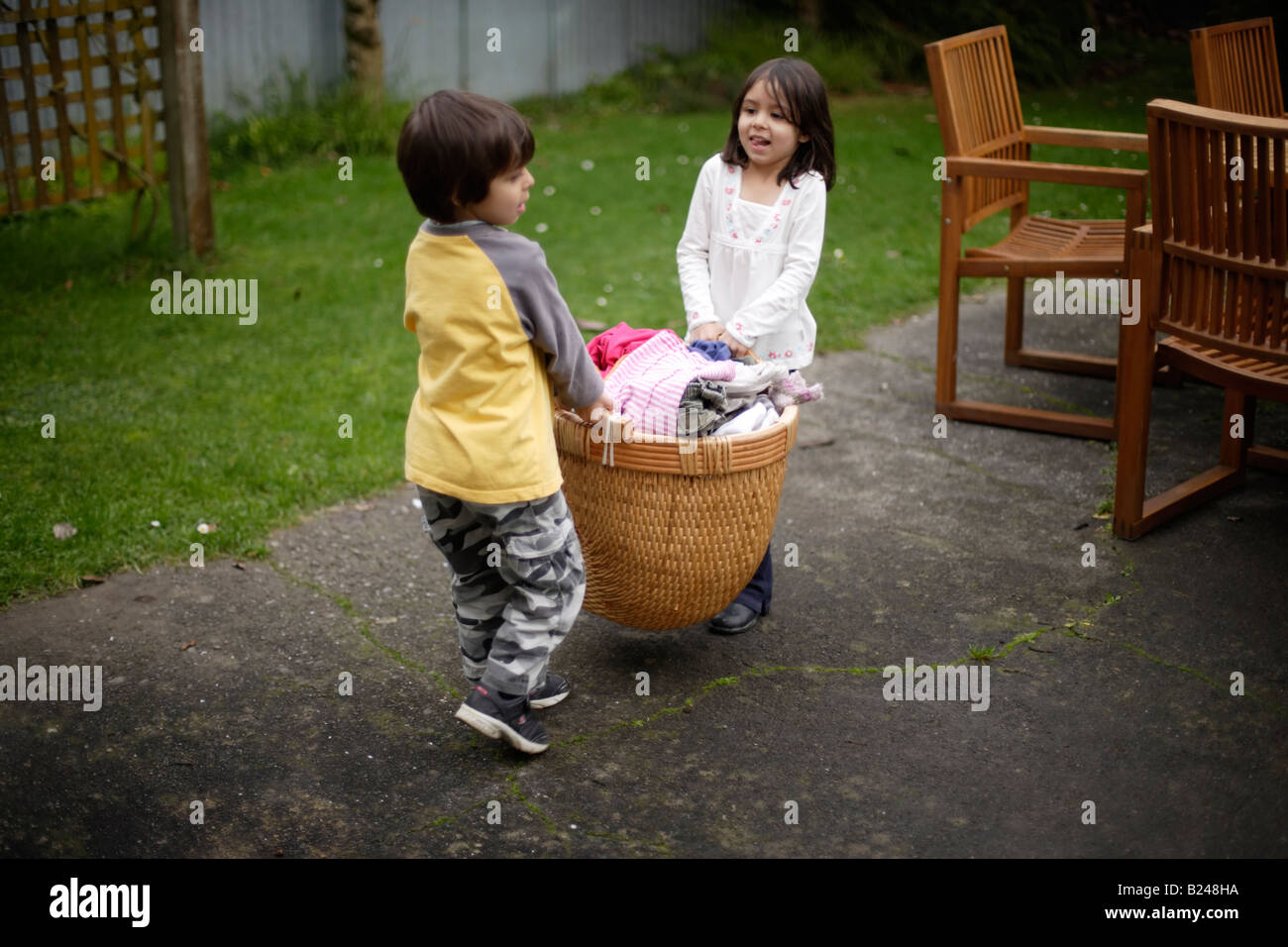 Mädchen im Alter von fünf und Bruder sechs Getrocknete Wäsche aus Zeile in einen Korb zu sammeln und bringen im Innenbereich Stockfoto