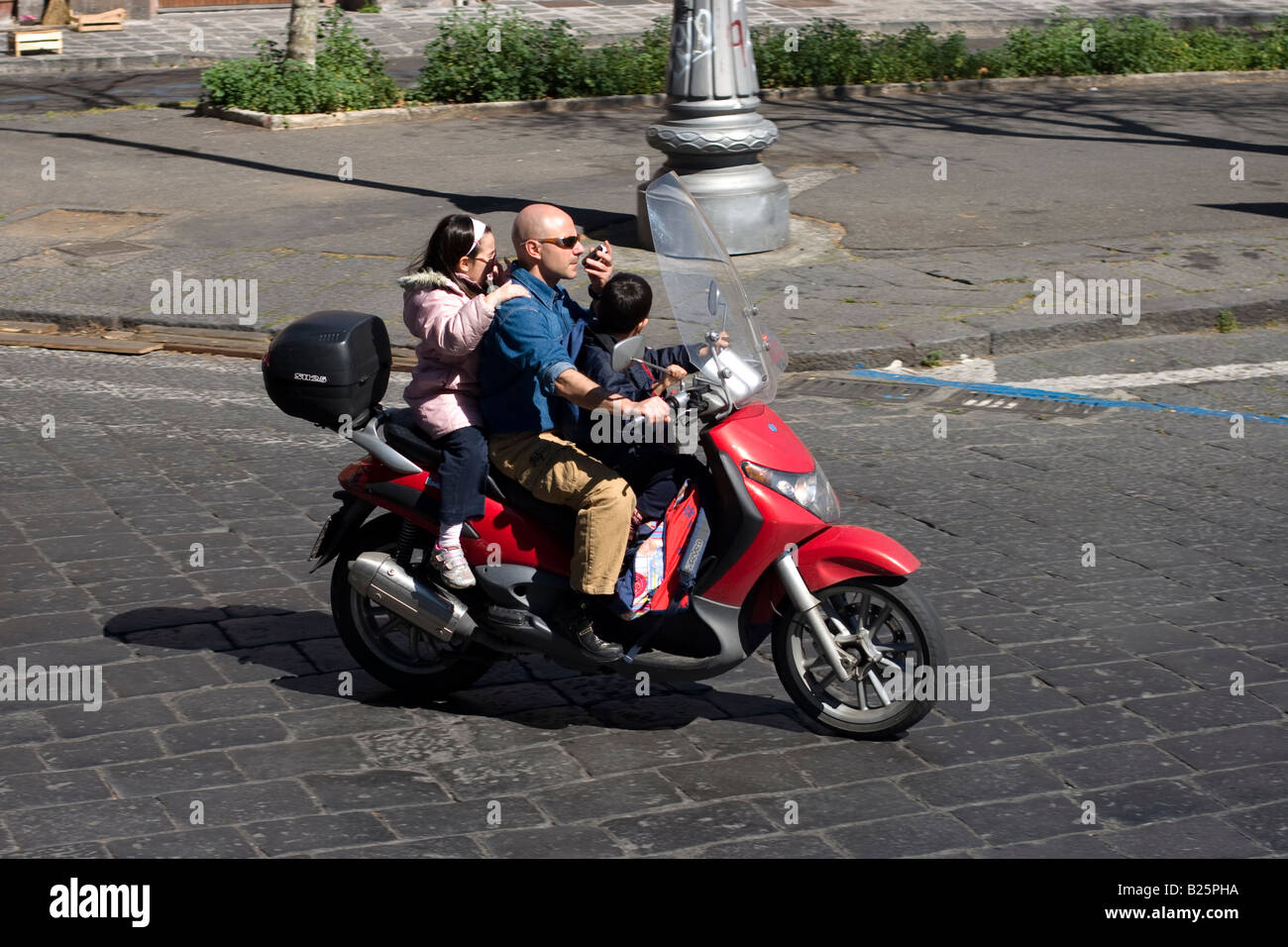 Mann fährt Motorrad mit seinen Kindern und Gespräche auf dem Handy in Catania, Sizilien, Italien Stockfoto