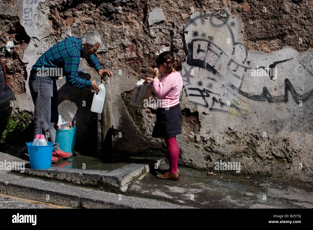 Ederly Mann und junges Mädchen holen Wasser bei einem öffentlichen Hahn in Catania, Sizilien, Italien Stockfoto