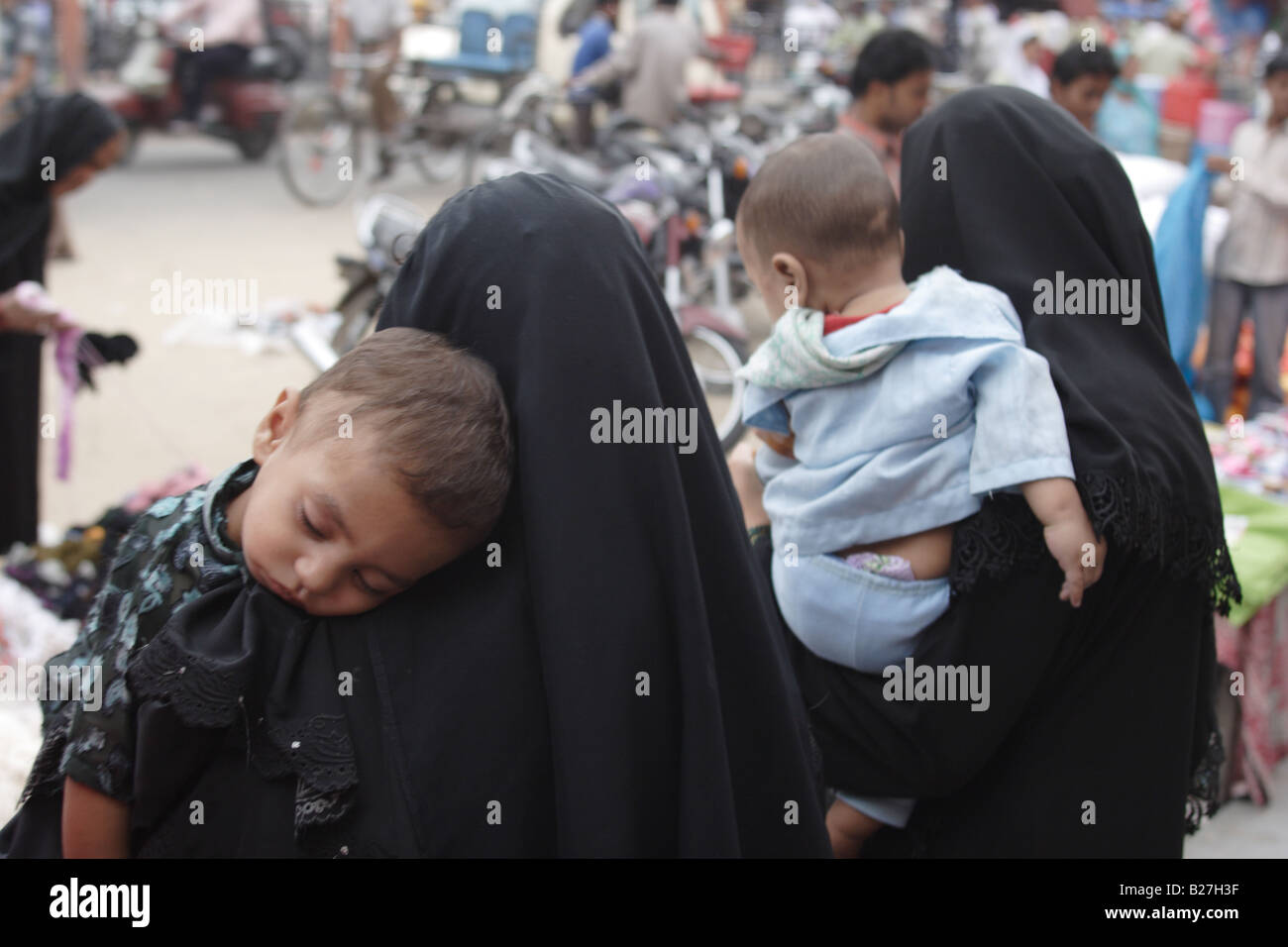 Zwei muslimische Frauen im Tschador mit ihren schlafenden Kindern auf einer Straße in Jaipur, Rajasthan, Indien. Stockfoto