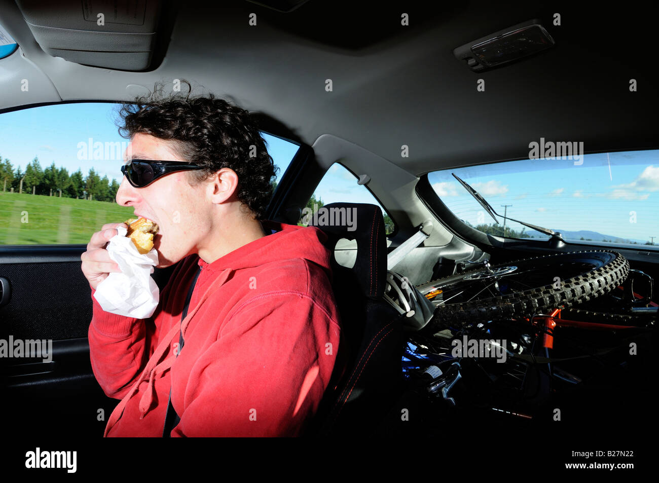 junger Mann, ein Auto zu fahren, während des Essens Stockfoto