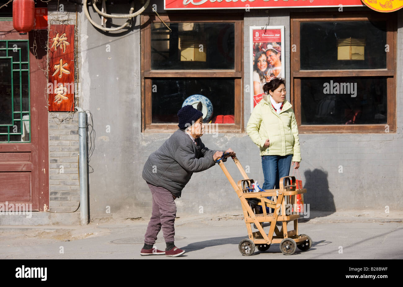 Ältere Frau schiebt hölzerne Warenkorb entlang der Fahrbahn im Bereich Hutongs Peking China Stockfoto