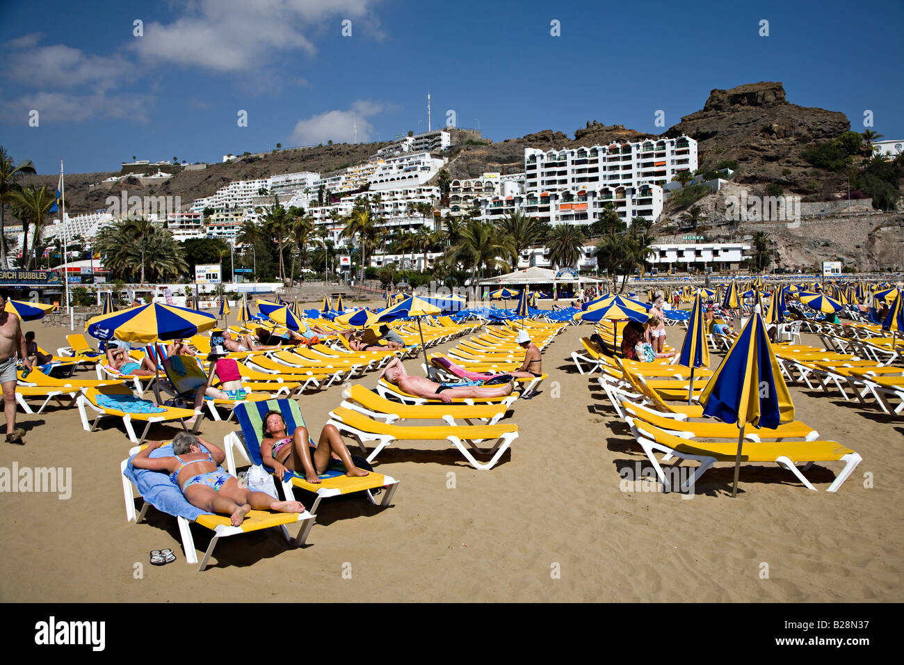 Menschen am Strand liegen mit Resort Ferienwohnungen auf Hügel Puerto