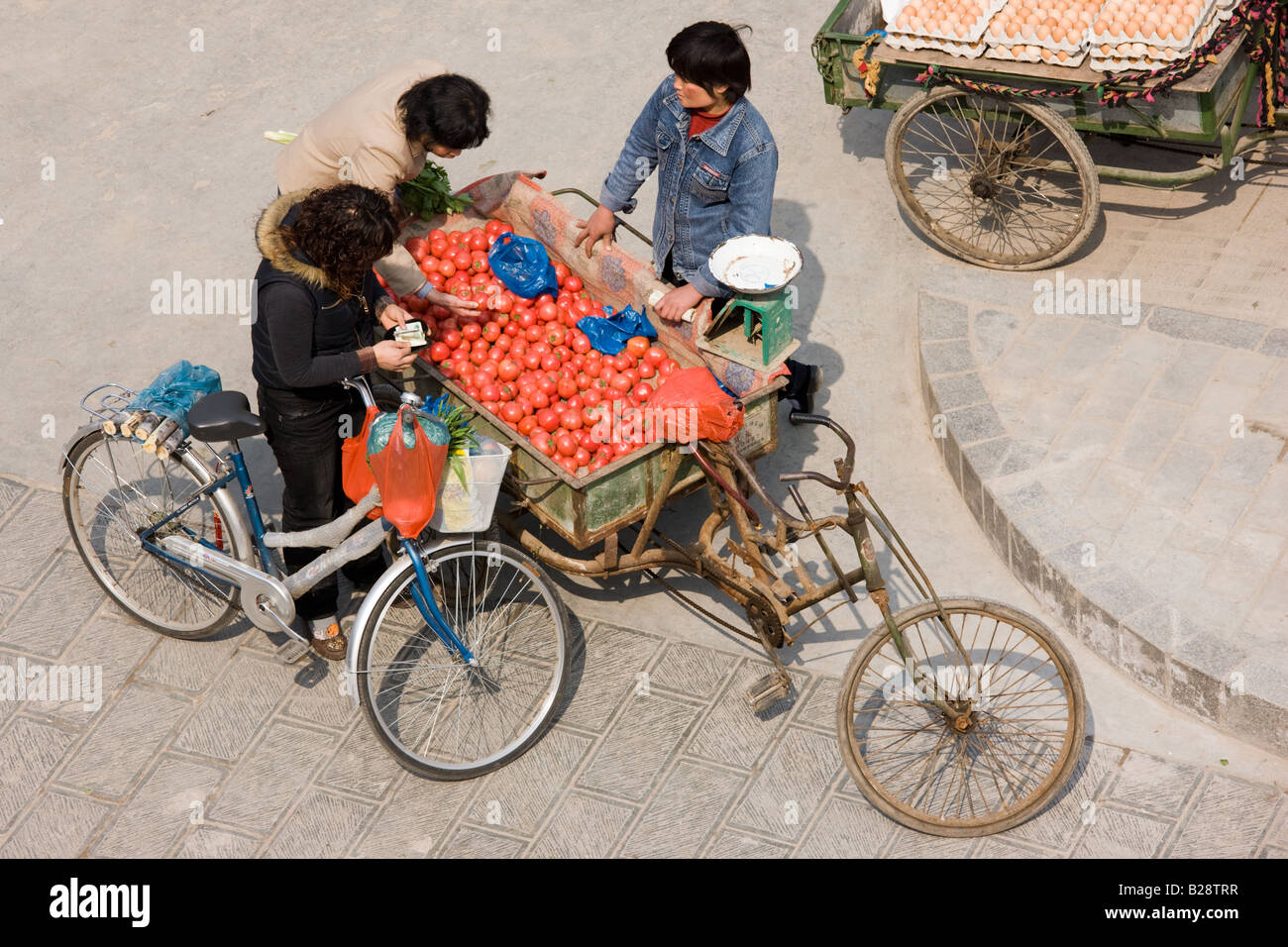 Frauen kaufen Tomaten aus dem Warenkorb in Straßenmarkt gesehen von der Stadt Mauer Xian China Stockfoto