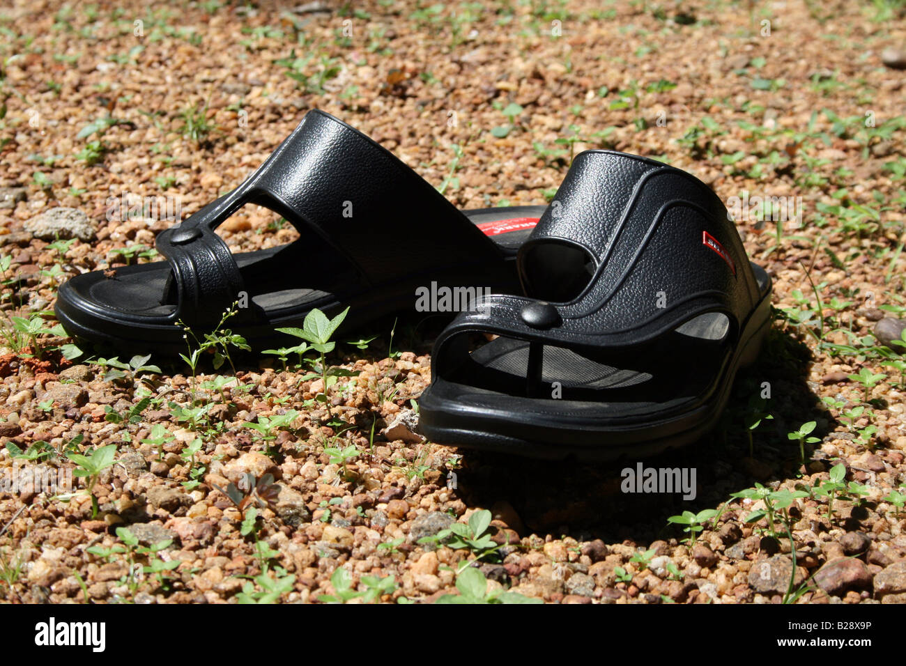 Schwarz offen toe Sandalen aus Leder hergestellt in Indien gehalten, um trocken unter der Sonne auf rauem Untergrund Steinchen Kies und Gras neue Stockfoto