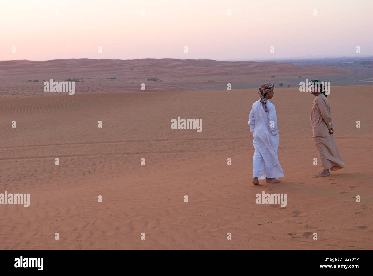 Beiden omanischen Männer reden, wie sie den Sonnenuntergang von einer Düne Wahiba Sands Stockfoto