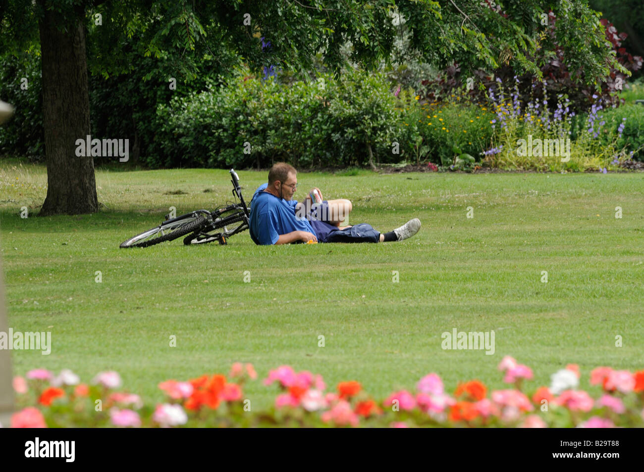 Menschen im Park: Ein müder Radfahrer nimmt eine Ruhe und trinken auf dem Rasen in Sheffield Botanical Gardens. Stockfoto