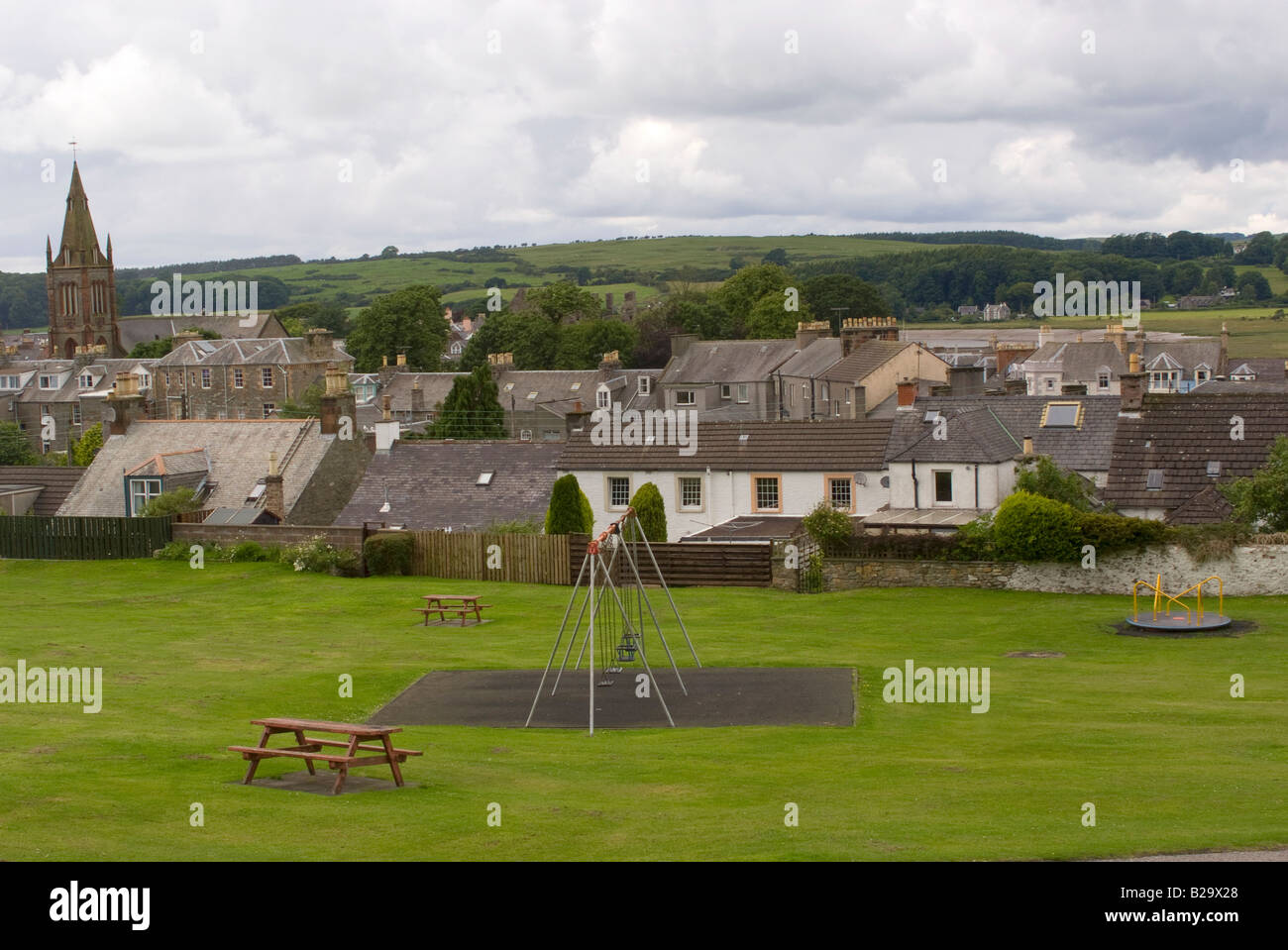 Leeren Spielplatz mit Kind schwingt und Kreisverkehr im Park mit Kirkcudbright Stadt im Hintergrund Dumfries und Galloway-Schottland Stockfoto