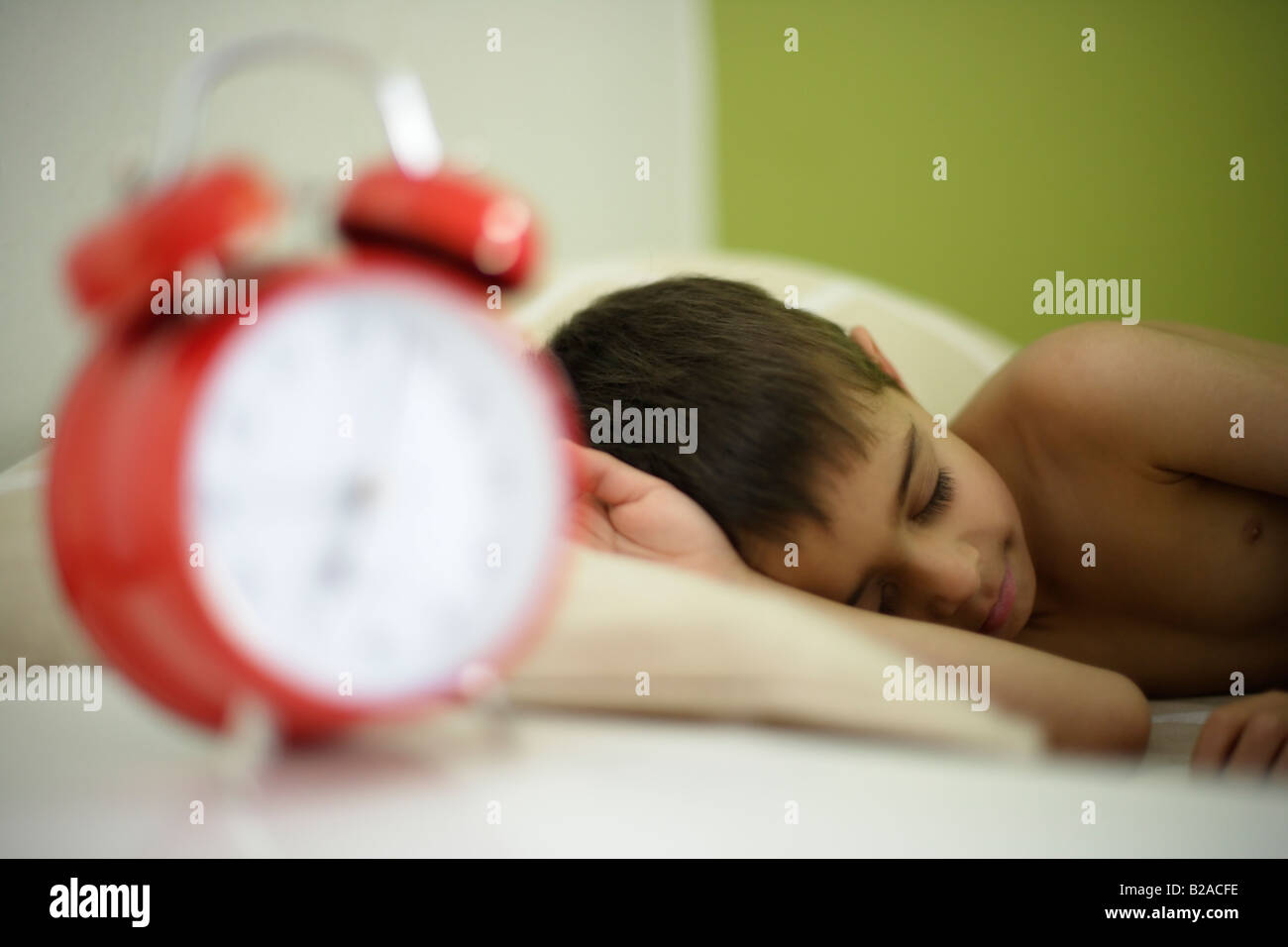 Junge Rennen im Alter von sechs schläft in seinem Bett neben hellen roten Wecker Mixed indischen Englisch Stockfoto