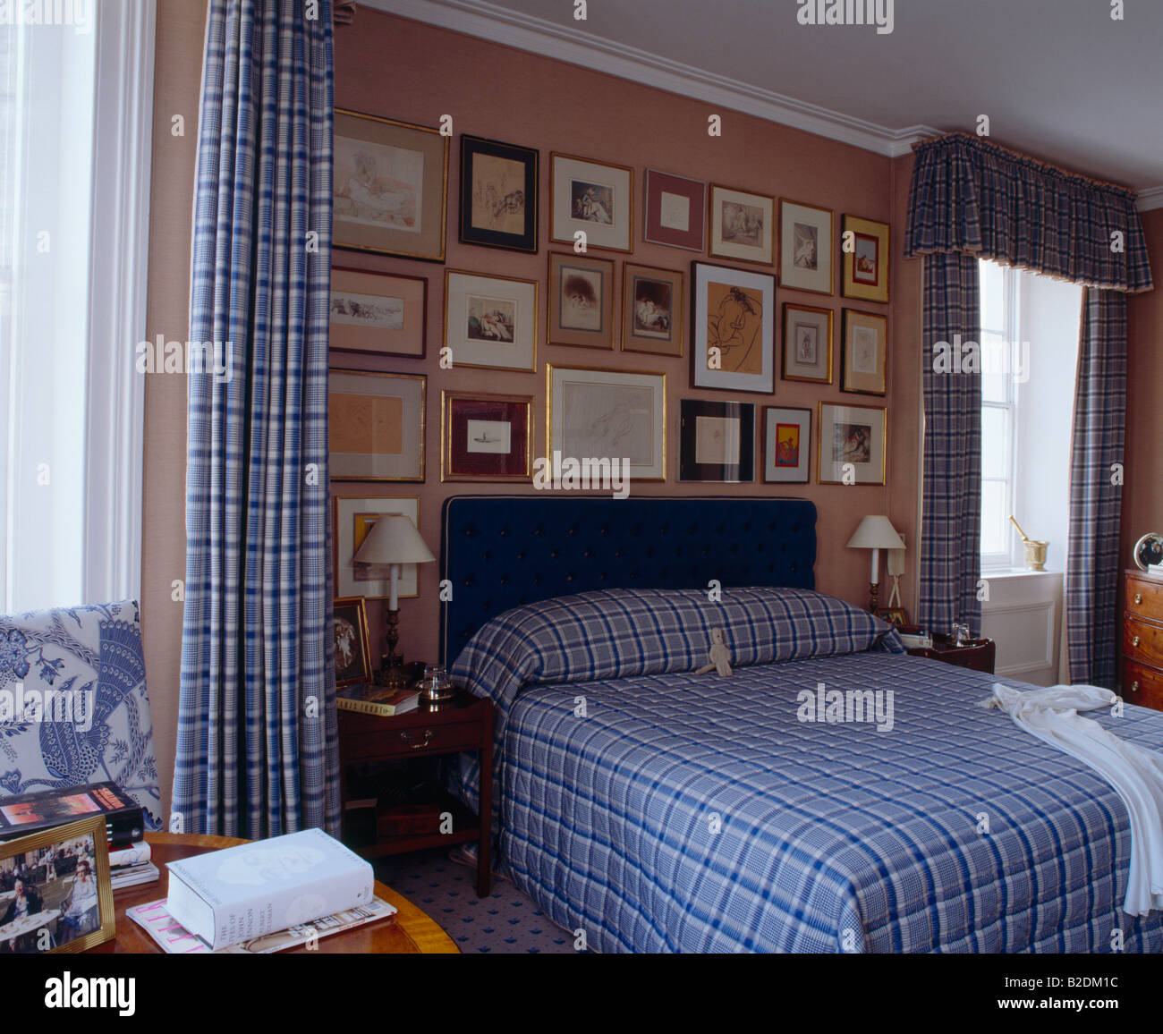 Blau kontrolliert Leinen- und passende Vorhänge in rosa Schlafzimmer mit Sammlung von Bilder über dem Bett Stockfoto